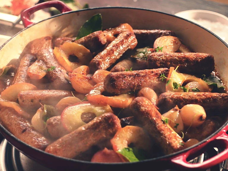 A casserole made with Quorn Sausages, shallots, and apples in a shallow Dutch oven.