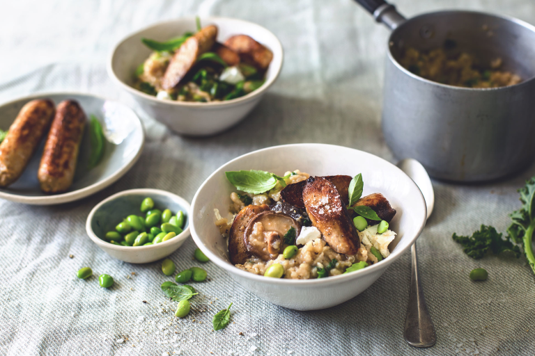 Risotto recipe made with Quorn Sausages, mushrooms and edamame served in a bowl with a side of edamame and 2 sausages on a plate