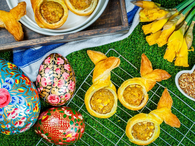Vegan bunny rolls served on a cooling rack with easter eggs and daffodils on the side.