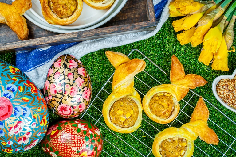 Vegan bunny rolls served on a cooling rack with easter eggs and daffodils on the side.