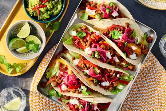 Six vegetarian tacos filled with Quorn mince, pickled red onion, pepper and lettuce in a dish. Served with sides of guacamole and lime wedges.