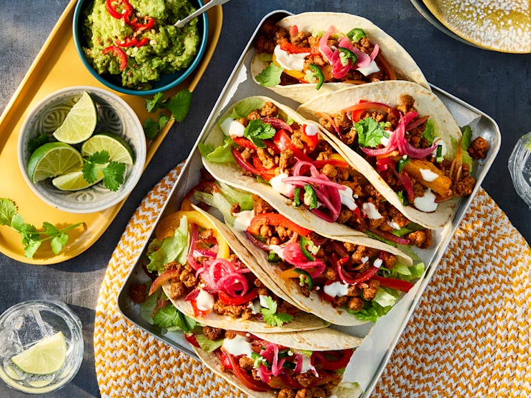 Six vegetarian tacos filled with Quorn mince, pickled red onion, pepper and lettuce in a dish. Served with sides of guacamole and lime wedges.