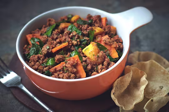 Spinach and sweet potato curry made with Quorn Grounds in an orange and white bowl with poppadums on the side.