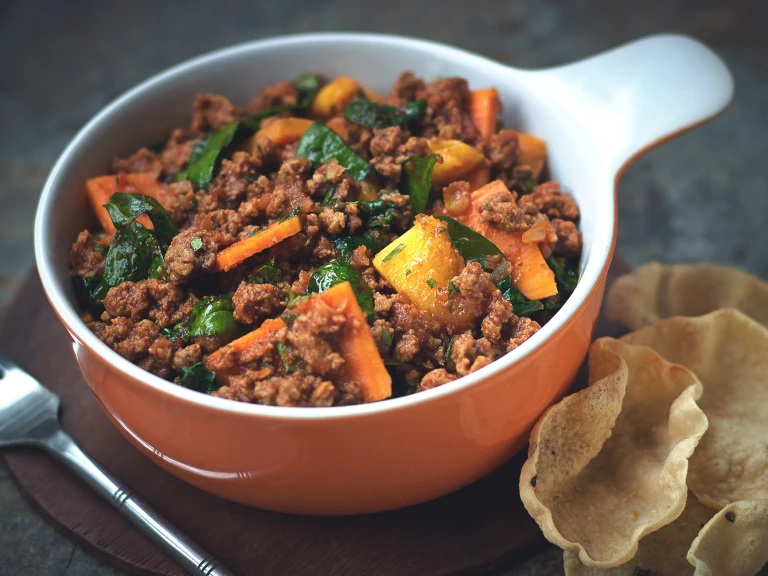 A casserole dish filled with Quorn Mince, Spinach and Sweet Potato Curry sat beside a serving of mini poppadums.