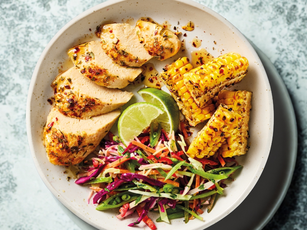 Quorn Cajun Fillets in a white bowl with lime, corn, cabbage and sugar snap peas.