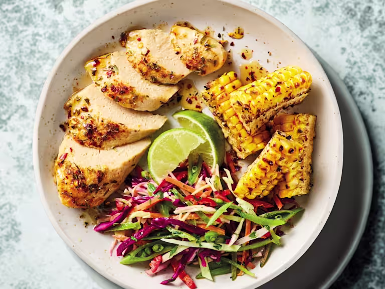 Quorn Cajun Fillets in a white bowl with lime, corn, cabbage and sugar snap peas.