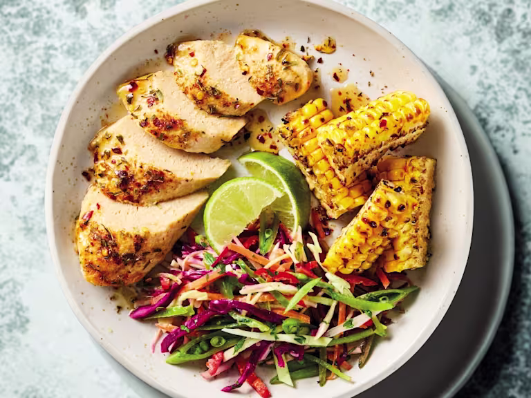 Quorn Cajun Fillets in a white bowl with lime, corn, cabbage and sugar snap peas.