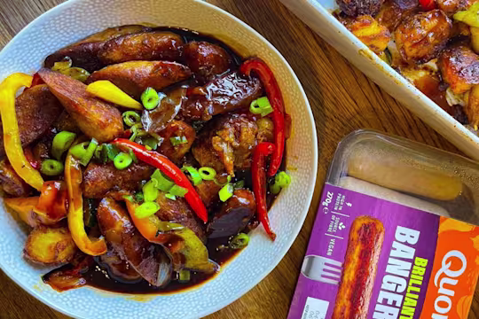 Potato bake served in a bowl positioned next to Quorn Brilliant Bangers vegan sausages