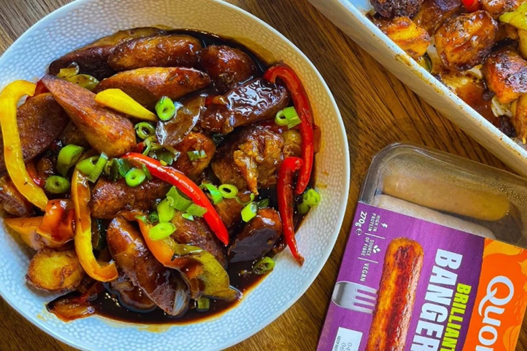 Potato bake served in a bowl positioned next to Quorn Brilliant Bangers vegan sausages