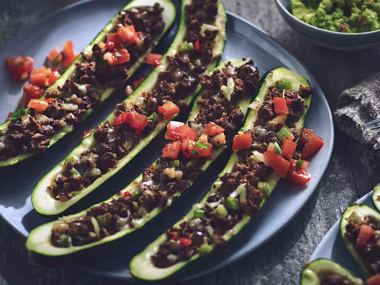 Four zucchini hollowed and filled with Quorn Grounds, cheese, and pico de gallo salsa on a blue plate.