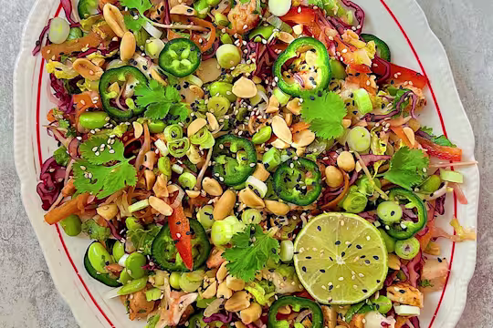 Chopped green and red salad on white plate with lime, spring onions, pepper and coriander