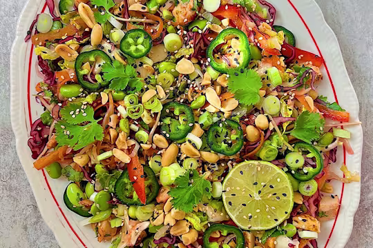 Chopped green and red salad on white plate with lime, spring onions, pepper and coriander