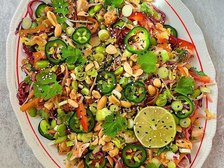 Chopped green and red salad on white plate with lime, spring onions, pepper and coriander