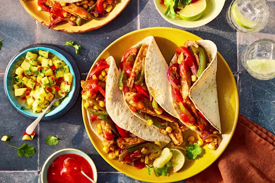 Quorn and Old El Paso vegetarian chicken tacos on a yellow plate with side dishes of mango alsa and sauce.