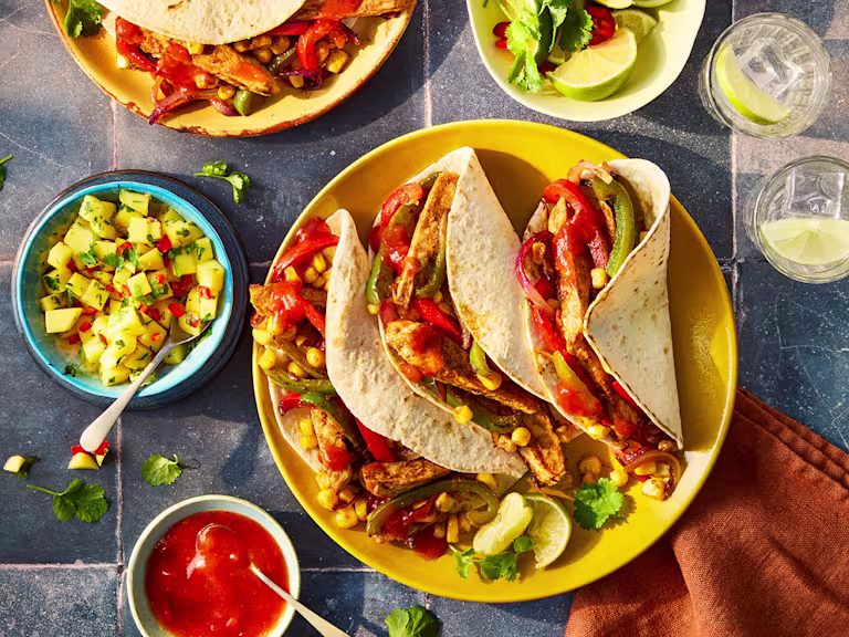 Quorn and Old El Paso vegetarian chicken tacos on a yellow plate with side dishes of mango alsa and sauce.