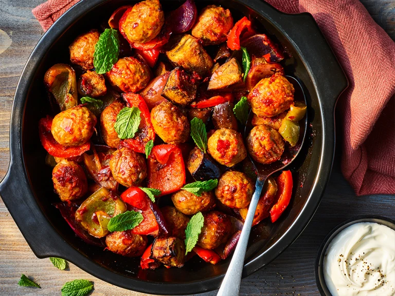 One pot harissa Quorn meatballs served in a black dish with crème fraiche on the side.