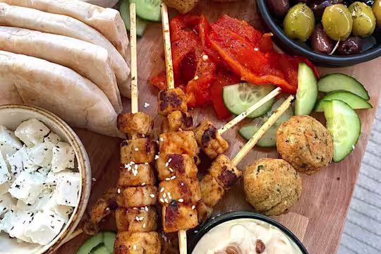 Skewered Quorn Vegan Pieces served with falafels, cucumber, peppers, olives, hummus, vegan tzatziki and pitta breads on a board.