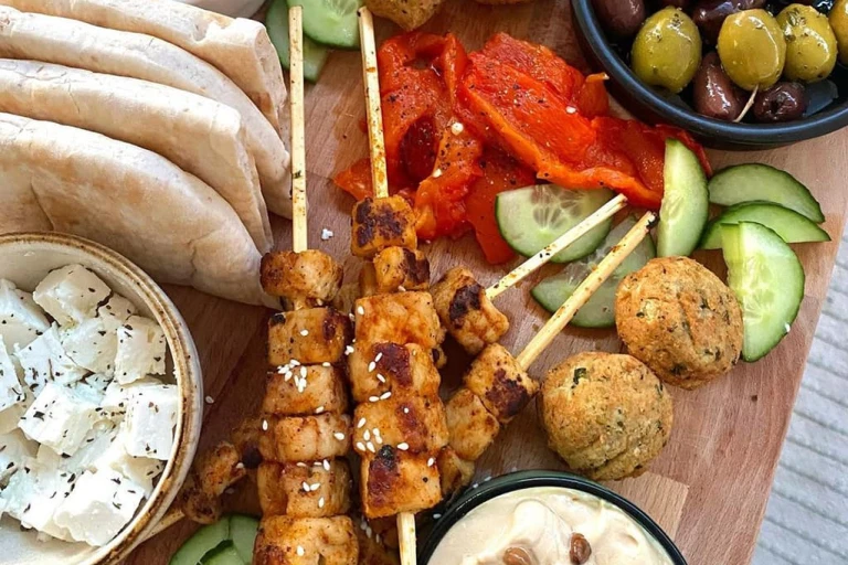 Skewered Quorn Vegan Pieces served with falafels, cucumber, peppers, olives, hummus, vegan tzatziki and pitta breads on a board.