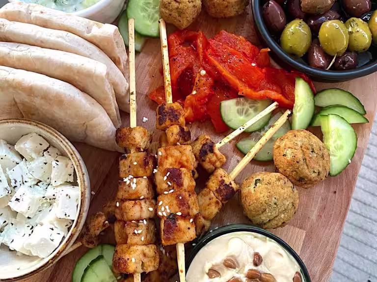 Skewered Quorn Vegan Pieces served with falafels, cucumber, peppers, olives, hummus, vegan tzatziki and pitta breads on a board.
