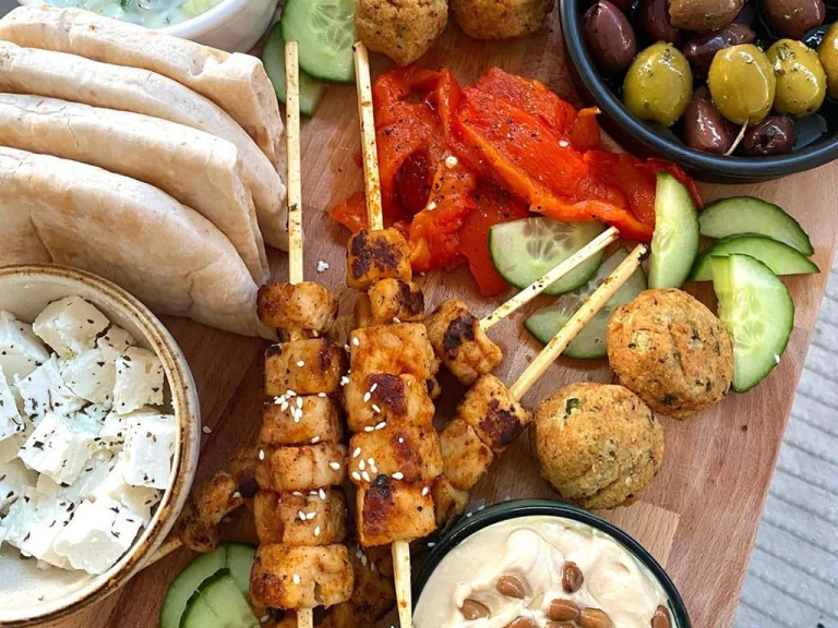 Skewered Quorn Vegan Pieces served with falafels, cucumber, peppers, olives, hummus, vegan tzatziki and pitta breads on a board.