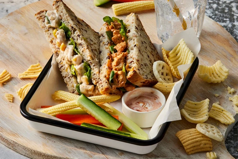 Two sandwiches, one Quorn Vegetarian BBQ Chicken and the other Quorn Vegetarian Chicken & Sweetcorn. They are both facing upwards to show the filling and are paired with veggie sticks and crisps. 