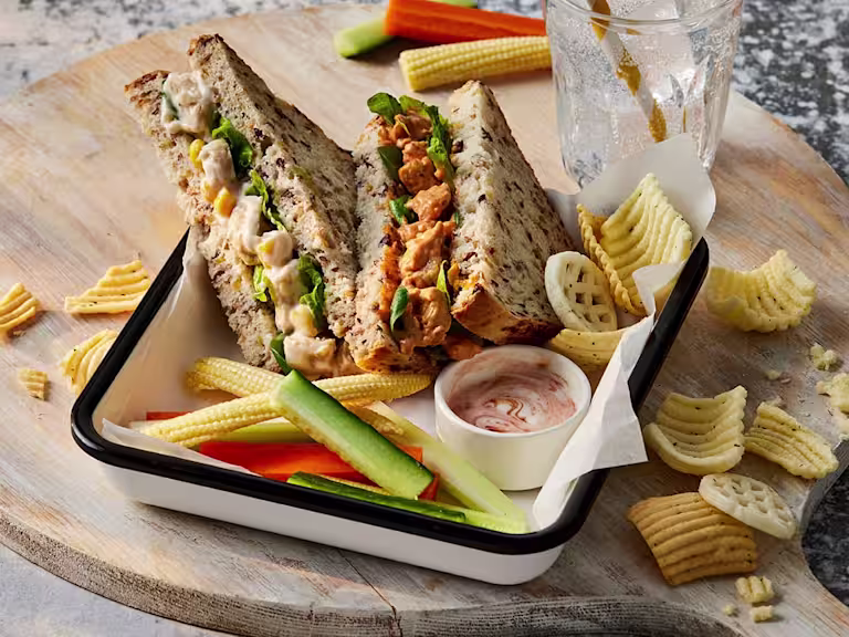 Two sandwiches, one Quorn Vegetarian BBQ Chicken and the other Quorn Vegetarian Chicken & Sweetcorn. They are both facing upwards to show the filling and are paired with veggie sticks and crisps.