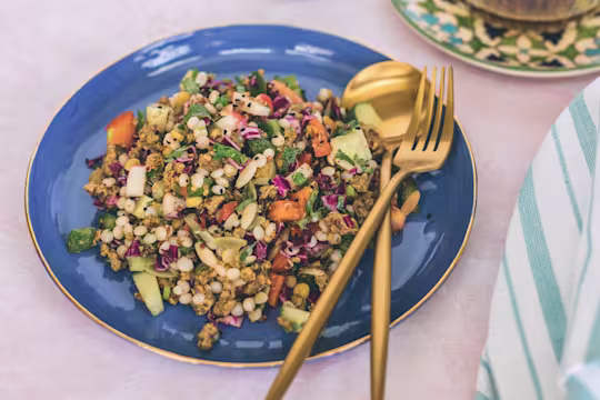 A grain salad with couscous, orzo, quinoa, chickpeas, pepper, radishes, cucumber and spiced Quorn Mince on a blue plate.
