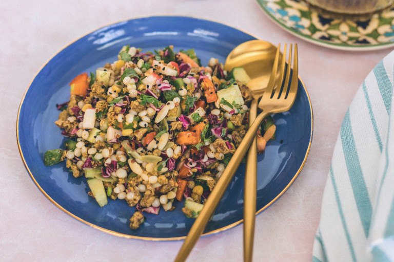 A grain salad with couscous, orzo, quinoa, chickpeas, pepper, radishes, cucumber and spiced Quorn Mince on a blue plate.