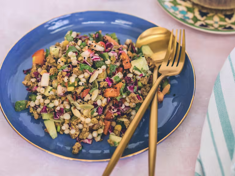 A grain salad with couscous, orzo, quinoa, chickpeas, pepper, radishes, cucumber and spiced Quorn Mince on a blue plate.