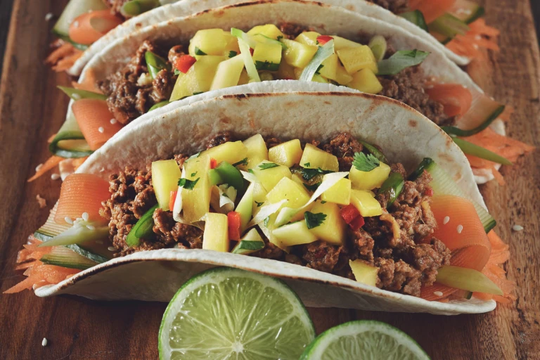 Three vegetarian Korean tacos made with flour tortillas filled with Quorn mince and pickled carrots and cucumbers and topped with mango salsa.