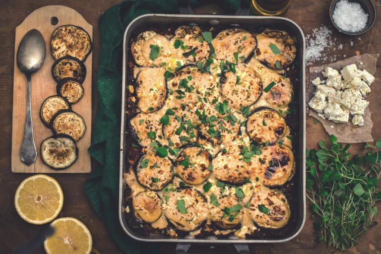 A vegetarian aubergine moussaka in a dish with one serving removed to show a filling of Quorn Mince.