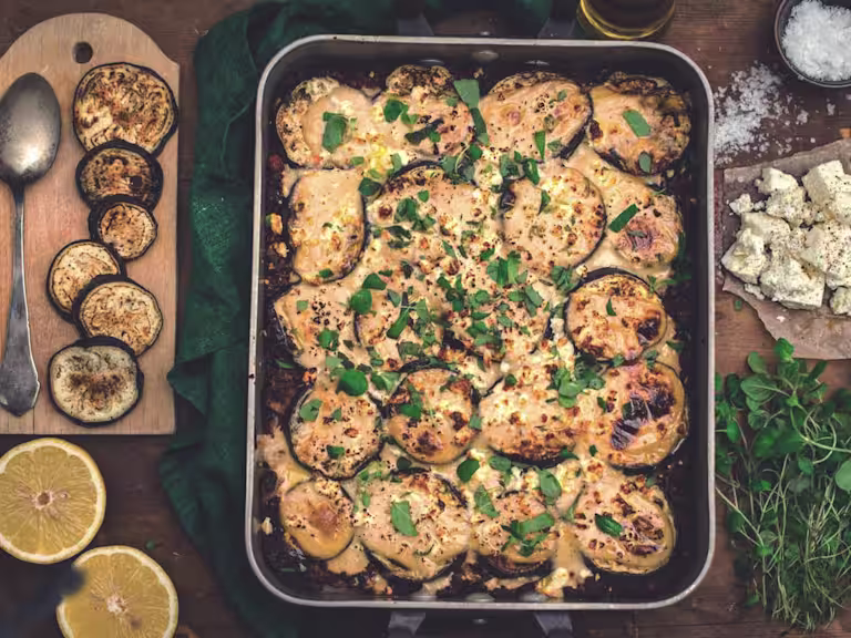 A vegetarian aubergine moussaka in a dish with one serving removed to show a filling of Quorn Mince.