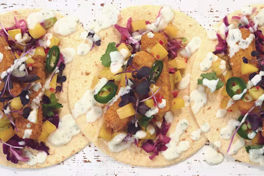 Tacos made with Quorn Vegan Fishless Fingers, jalapenos, diced mango and red cabbage served on tortillas drizzled with yoghurt