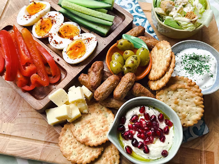 A Summer Snack Plate with Quorn Cocktail Sausages, cheese, crackers, boiled eggs, peppers, cucumber, olives, tzatziki and hummus.