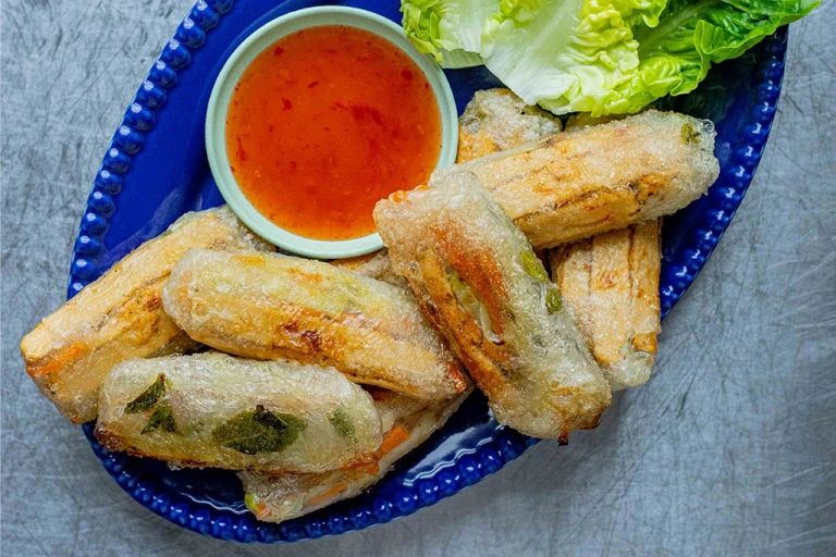 Sweet Chilli Quorn Vegan Spring Rolls served with a side of sauce and lettuce leaves on a blue dish.