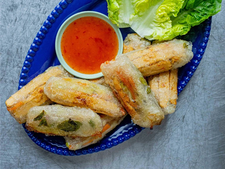 Sweet Chilli Quorn Vegan Spring Rolls served with a side of sauce and lettuce leaves on a blue dish.