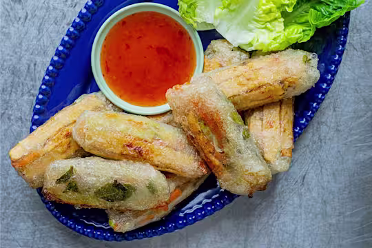 Sweet Chilli Quorn Spring Rolls served with a side of sauce and lettuce leaves on a blue dish.