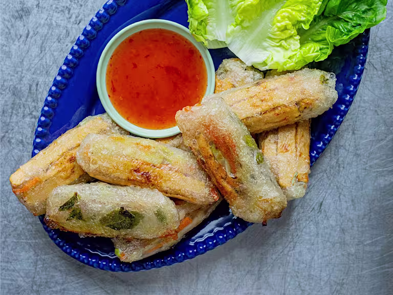 Sweet Chilli Quorn Spring Rolls served with a side of sauce and lettuce leaves on a blue dish.