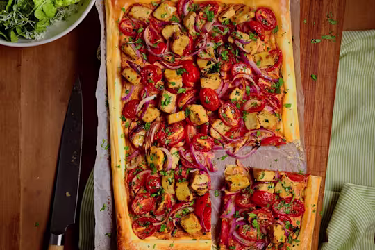 Quorn Vegetarian Chicken Pesto & Tomato Tart displaying all the toppings including Quorn Pieces, tomatoes and red onions sitting on top of a baking sheet.