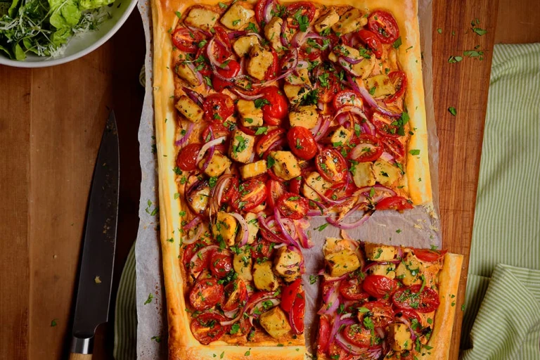 Quorn Vegetarian Chicken Pesto & Tomato Tart displaying all the toppings including Quorn Pieces, tomatoes and red onions sitting on top of a baking sheet.