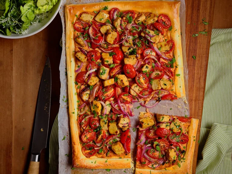 Quorn Vegetarian Chicken Pesto & Tomato Tart displaying all the toppings including Quorn Pieces, tomatoes and red onions sitting on top of a baking sheet.