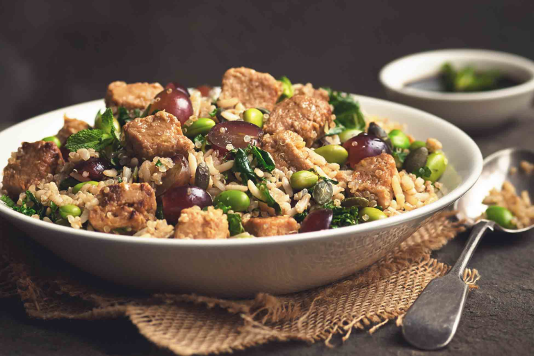 A quinoa salad with edamame, rice, halved grapes, kale, and Quorn Pieces in a white bowl.