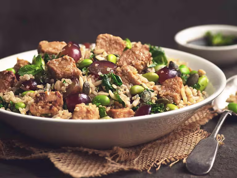 A bowl of Quorn Vegan Pieces & Quinoa Salad placed beside a spoon and a bowl of dressing.