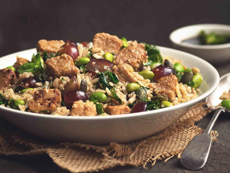 A quinoa salad with edamame, rice, halved grapes, kale, and Quorn Pieces in a white bowl.