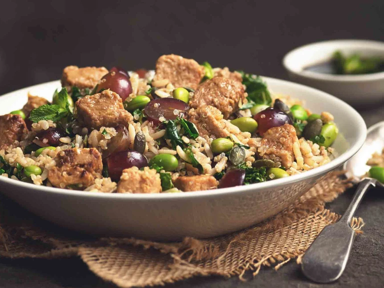 A bowl of Quorn Vegan Pieces & Quinoa Salad placed beside a spoon and a bowl of dressing.