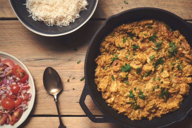 En kastrull fylld med currygryta, en tallrik med sallad, en skål med ris, och en sked bredvid.