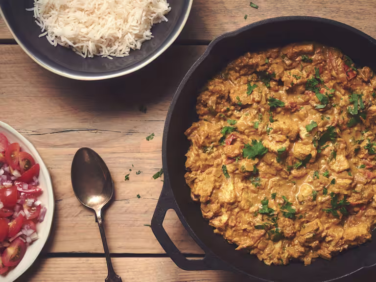 En kastrull fylld med currygryta, en tallrik med sallad, en skål med ris, och en sked bredvid.