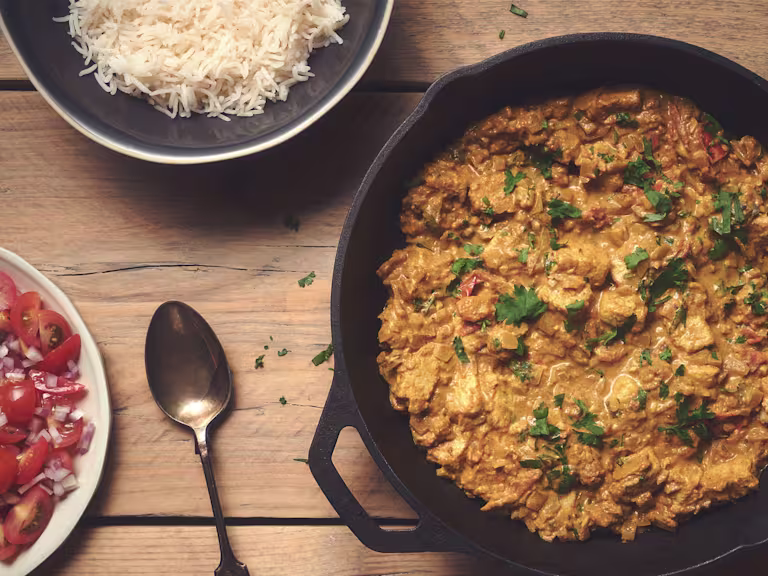 Quorn vegetarian chicken pieces curry served in a black dish with a side of rice.