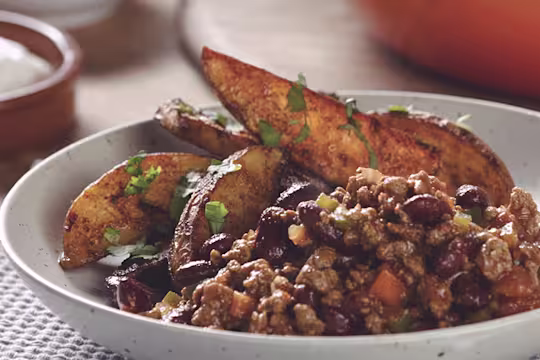 A bowl of Quorn Mince and kidney bean chilli with potato wedges on the side.