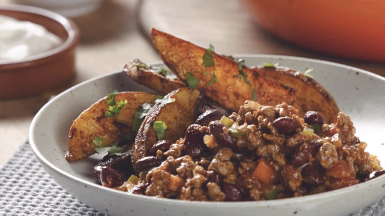 A bowl of Quorn Mince and kidney bean chilli with potato wedges on the side.